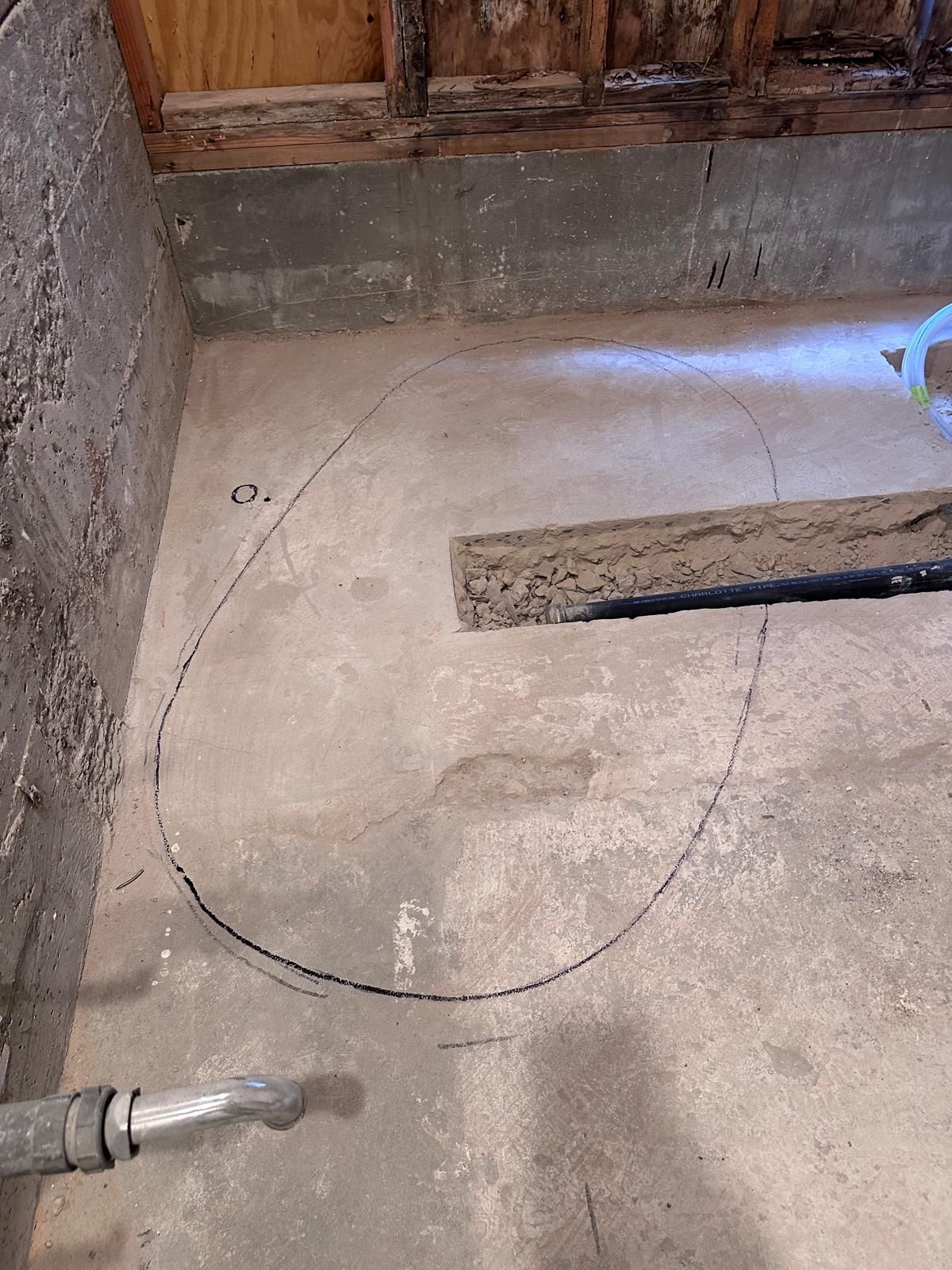 Concrete floor with a narrow trench cut open for a drain line and a curved outline drawn where the next cut will go