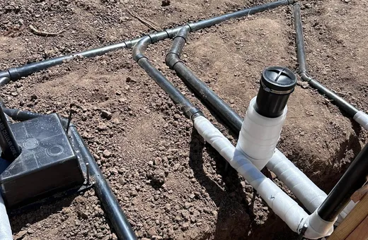 Black drain lines with wrapped fittings and capped cleanout risers laid in the soil before a slab is poured